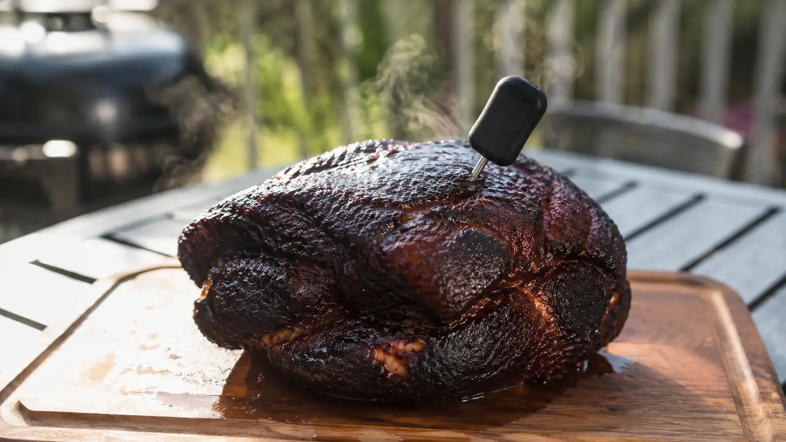 A finished pork shoulder with dark glossy bark resting on a wooden cutting board, steam rising, morning light across the patio