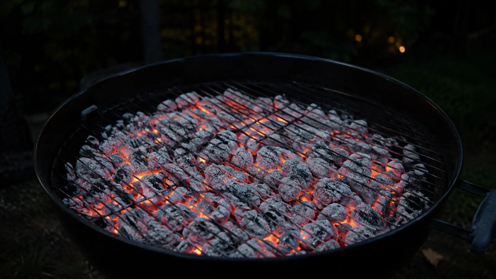 A bed of white-ashed charcoal dumped from a chimney into a kettle grill, arranged in an even layer with orange glow ready for cooking